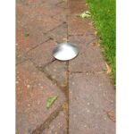 A stainless steel demarcation stud on the ground next to a grassy area, resembling a warrior.