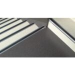 A close up of a stair with a metal railing and Warrior Stair Nosing.