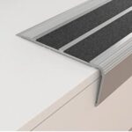 A stainless steel stair tread with Warrior Stair Nosing on top of a white counter.