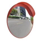 The Warrior 60CM Convex Mirror WAR-CM60-PM, resembling a warrior's shield, reflects the surrounding scenery as a vibrant red circle on the side of the road.