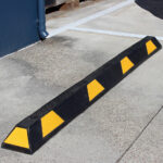 A Warrior Rubber Stopper 100MM Height 150MM Width 1800MM Length with Yellow Strip parked on the side of the road.