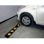 A white car, equipped with a Warrior Rubber Stopper 100MM Height 150MM Width 550MM Length With Yellow Strip, is parked in a parking lot.